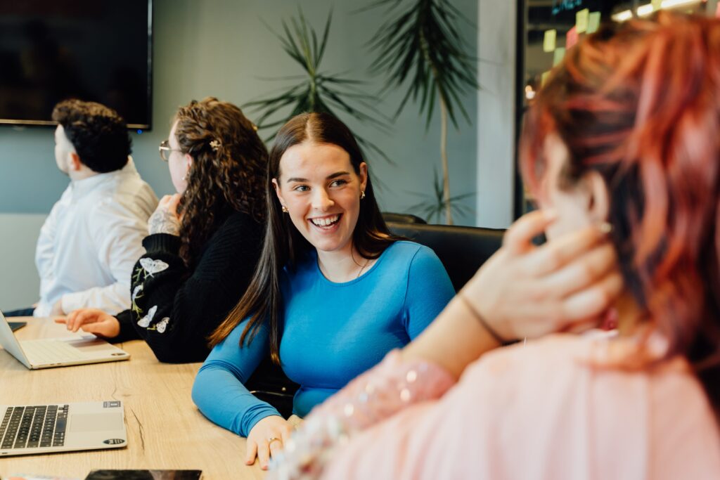 Maddie in a blue long sleeve t shirt smiling at colleague